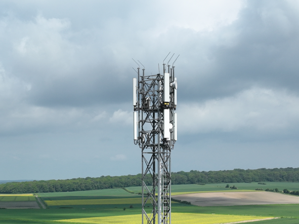 Mobilfunkmast Inspektion Mobilfunkmasten auf einem Feld mit Bergen im Hintergrund.